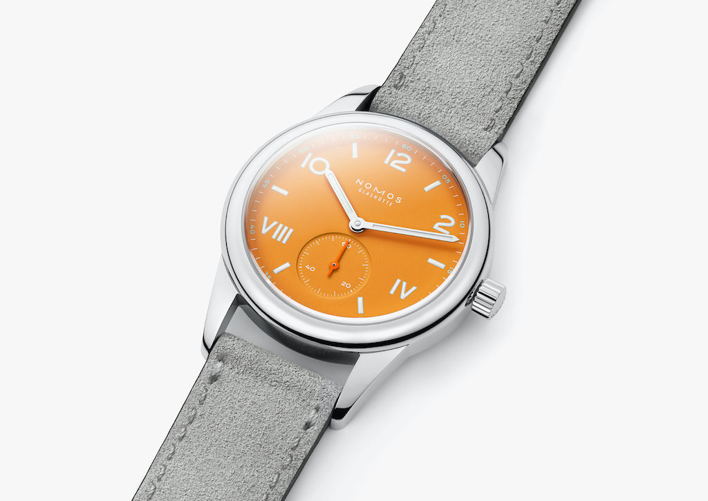 The gray strap made of soft velour leather creates a gentle contrast to the striking orange of the dial.